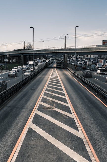 An empty toll plaza on a wide road with multiple lanes, including designated lanes for vehicle passage and a low height barrier with red and white stripes. The lanes are clearly marked with white line