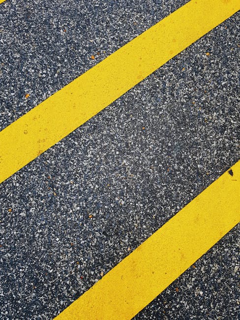 Close-up view of a section of rough asphalt pavement with two bold yellow diagonal lines painted on it, likely marking a designated area for moving or parking during a house removal or furniture transport operation. The surface shows signs of use with small stones and gravel visible, and the yellow lines are slightly worn, indicating frequent use. This scene may be part of a narrow street or alley used by Man with Van Turnpike Lane for home relocation services, highlighting the importance of navigating tight urban streets safely while loading or unloading moving vehicles such as vans. The image emphasizes the logistical considerations involved in parking and access during furniture transport and packing and moving processes, especially in confined street environments typical for house removals in central or densely populated areas.