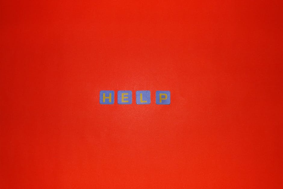 Close-up image of four small blue alphabet blocks with yellow outlines spelling the word 'HELP' arranged in a horizontal line on a bright red background. The blocks are evenly spaced and centered in the frame, with the vibrant background providing high contrast to the blocks. This clear, detailed image highlights the concept of urgent assistance or support, which may relate to home evacuation or moving services offered by companies like Man with Van Turnpike Lane during emergency relocations or same-day removals.